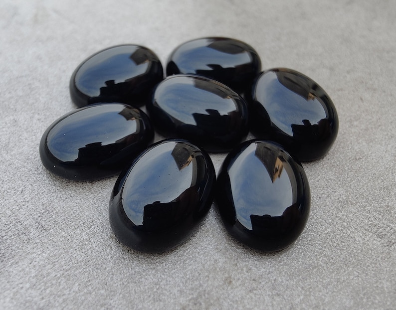 May include: A group of seven oval-shaped black gemstones. The gemstones are smooth and polished, with a glossy finish.