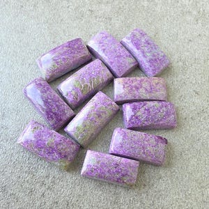 May include: A collection of ten rectangular, polished cabochons featuring a vibrant purple and muted green mottled pattern. Each stone has a smooth, rounded surface with a glossy finish, displaying unique natural veining and colour variations.