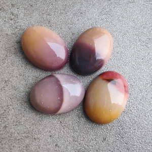 May include: Four oval-shaped, polished stones with different color patterns. The stones are a mix of brown, pink, purple, and white.