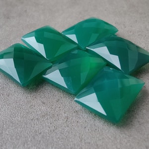 Pode incluir: Um grupo de sete cabochões de pedras preciosas verdes, cortados em forma quadrada com bordas biseladas. As pedras estão dispostas em uma pilha solta, com algumas sobrepostas.