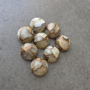 May include: A collection of eight round, polished stones. The stones have a creamy white base color with intricate patterns of gold and brown veining. The stones are arranged in a circular pattern.