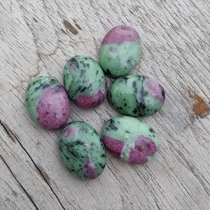 Könnte beinhalten: Sechs ovale, grün-rosa Steine mit einem marmorierten Muster. Die Steine sind glatt und poliert.