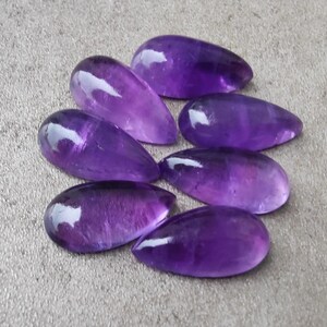 Op de afbeelding: Zeven paarse amethist edelstenen cabochons in een traanvorm.