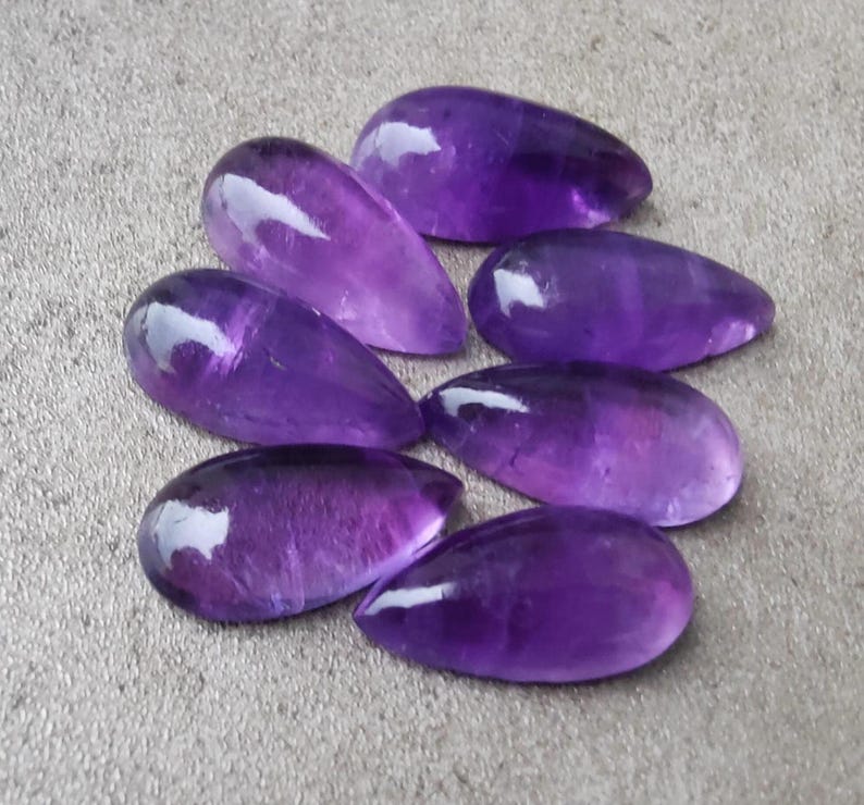 Op de afbeelding: Zeven paarse amethist edelstenen cabochons in een traanvorm.
