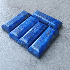 Könnte beinhalten: Fünf rechteckige Stücke polierten Lapislazuli, ein tiefblauer Edelstein mit goldenen Pyritflocken. Die Steine sind in einem Stapel angeordnet, wobei das größte Stück unten und das kleinste Stück oben liegt.