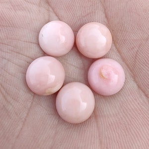 Puede incluir: Cinco piedras preciosas redondas, rosadas y en cabujón. Las piedras preciosas son lisas y pulidas.