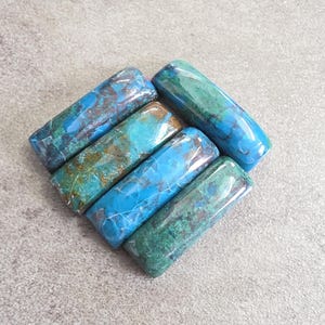 Puede incluir: Cuatro piedras preciosas pulidas de forma rectangular dispuestas en grupo. Cada piedra presenta un patrón jaspeado único con tonos vibrantes de turquesa, azul profundo y verde bosque, caracterizadas por superficies lisas y brillantes.