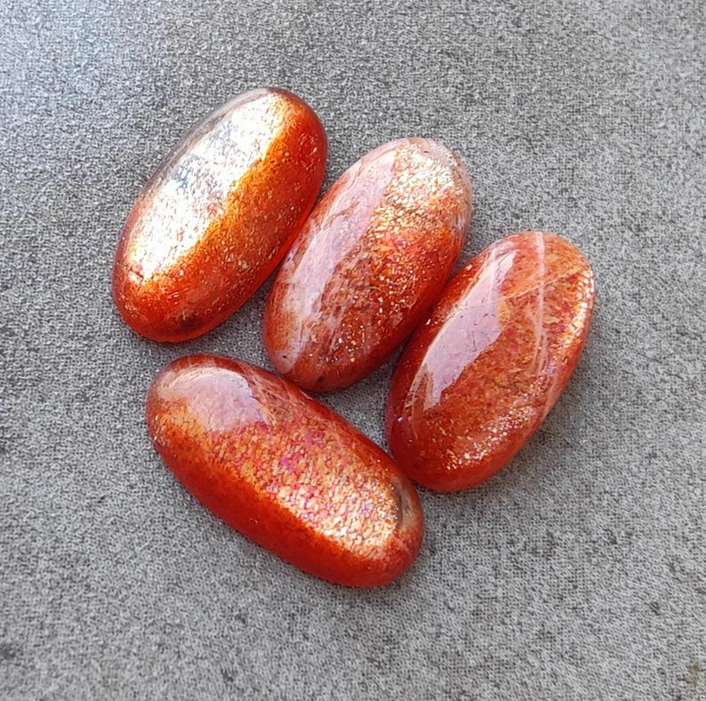 K&ouml;nnte beinhalten: Vier ovale Sonnenstein-Cabochons mit schimmerndem, irisierendem Finish. Die Steine sind eine Mischung aus Orange, Rot und Gold.