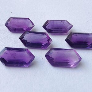 K&ouml;nnte beinhalten: Sechs facettierte, sechseckige Amethyst-Edelsteine. Die Edelsteine haben eine tiefviolette Farbe und sind auf einer wei&szlig;en Oberfl&auml;che angeordnet. Die Facetten fangen das Licht ein und erzeugen Glanzlichter und Schatten. Geeignet f&uuml;r die Schmuckherstellung.