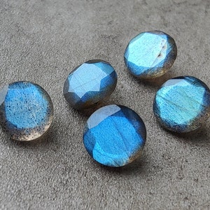 May include: Five iridescent blue labradorite gemstone cabochons with a faceted finish. The stones have a dark blue to light blue color with a hint of green.