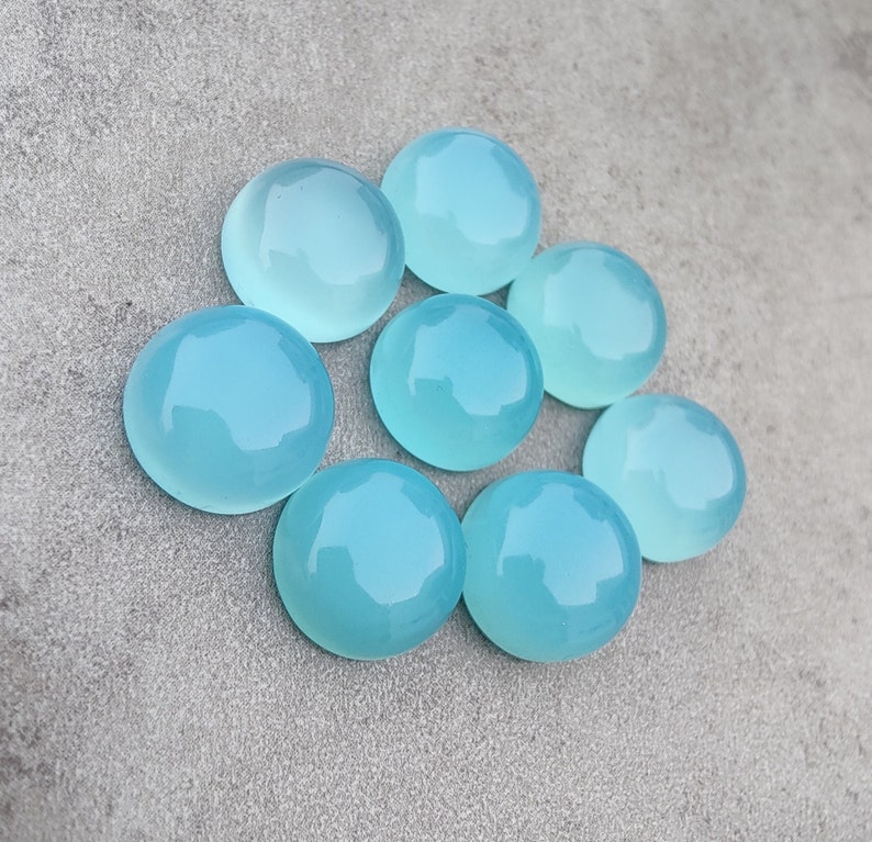 Pu&ograve; includere: Otto pietre preziose rotonde, lisce e di colore blu chiaro a cabochon. Le pietre sono disposte in cerchio su uno sfondo grigio.