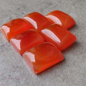 May include: Six polished, rectangular orange gemstones arranged in a diamond pattern. The stones have rounded edges and a glossy finish, reflecting light. The gemstones are set against a neutral gray background.