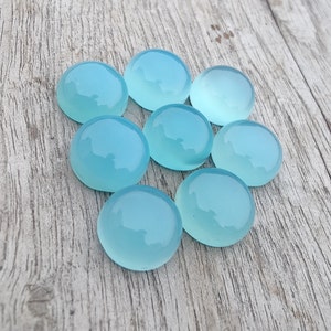 Pu&ograve; includere: Otto pietre preziose rotonde di cabochon blu chiaro su una superficie di legno.