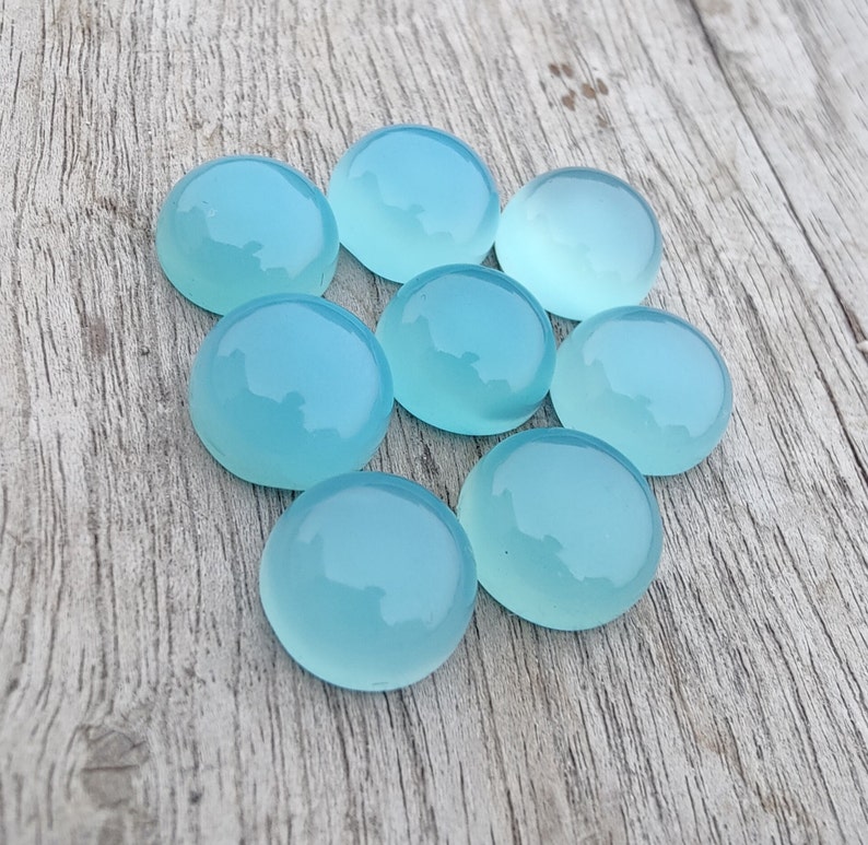 Pu&ograve; includere: Otto pietre preziose rotonde di cabochon blu chiaro su una superficie di legno.