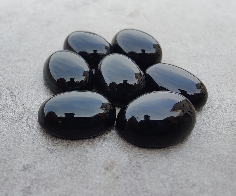 May include: Seven smooth, oval-shaped black gemstones. The stones are polished and have a glossy finish.
