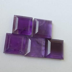 Peut inclure: Cinq pierres pr&eacute;cieuses d'am&eacute;thyste taill&eacute;es en carr&eacute;, de diff&eacute;rentes nuances de violet. Les pierres sont dispos&eacute;es en l&eacute;ger chevauchement, mettant en valeur leurs surfaces facett&eacute;es et leur couleur riche. Les pierres sont taill&eacute;es avec pr&eacute;cision.