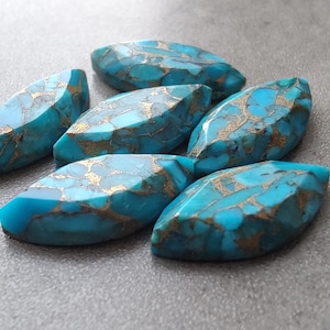 May include: Seven turquoise cabochon stones with gold flecks, shaped like elongated ovals, arranged on a gray surface.