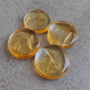 May include: Four round, translucent, amber-colored glass pieces with gold flecks. The pieces are smooth and have a slightly rounded edge.