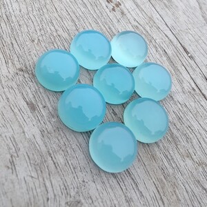 Pu&ograve; includere: Otto pietre preziose rotonde di cabochon blu chiaro su una superficie di legno chiaro.