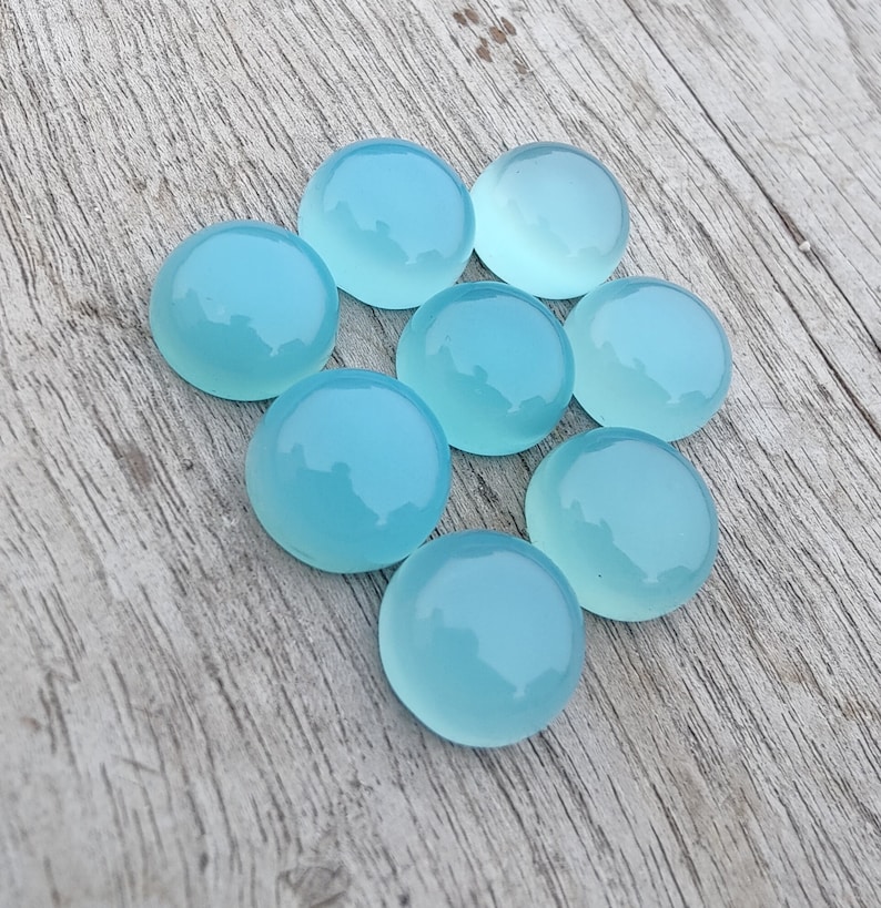 Pu&ograve; includere: Otto pietre preziose rotonde di cabochon blu chiaro su una superficie di legno chiaro.