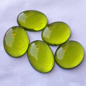 May include: Five oval-shaped, translucent green glass stones. The stones are smooth and shiny.