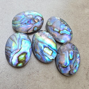 May include: Five oval-shaped abalone shells with iridescent blue, green, and purple hues. The shells have a smooth, polished surface and display a swirling pattern of colors. These shells are suitable for jewelry making or decorative purposes.