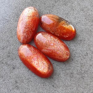 K&ouml;nnte beinhalten: F&uuml;nf ovale Cabochons aus Sunstone mit einer rot-orangenen Farbe und einem glitzernden, irisierenden Finish.