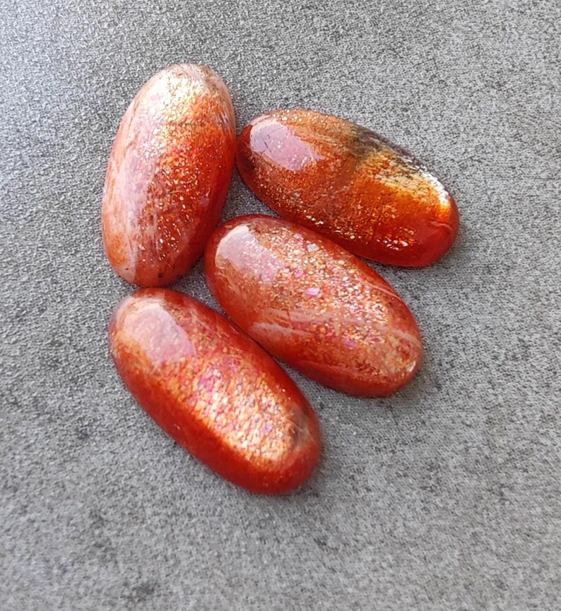 K&ouml;nnte beinhalten: F&uuml;nf ovale Cabochons aus Sunstone mit einer rot-orangenen Farbe und einem glitzernden, irisierenden Finish.