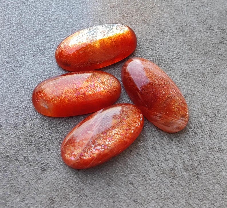 K&ouml;nnte beinhalten: Vier ovale Cabochons aus Sunstone mit schimmerndem, irisierendem orange-goldenen Finish.
