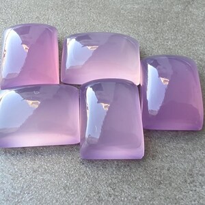 Pu&ograve; includere: Cinque pietre preziose rettangolari lucide in varie tonalit&agrave; di lavanda e viola. Le pietre hanno bordi arrotondati e una superficie lucida e riflettente. Le pietre sono disposte su una superficie grigia.