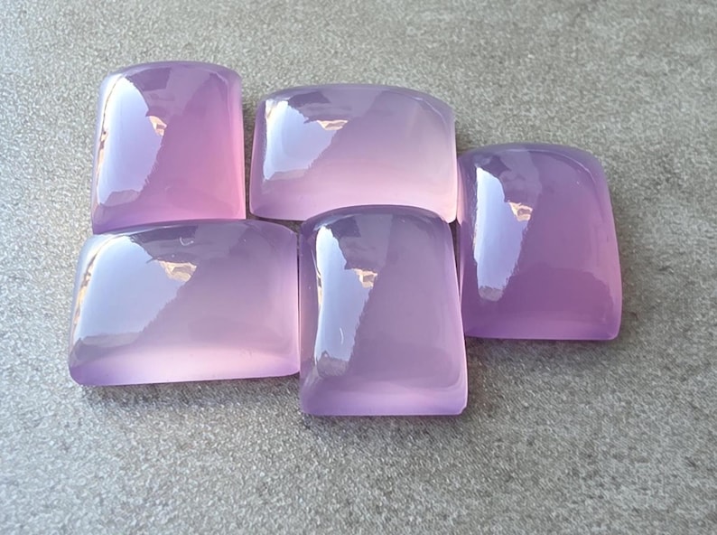 Pu&ograve; includere: Cinque pietre preziose rettangolari lucide in varie tonalit&agrave; di lavanda e viola. Le pietre hanno bordi arrotondati e una superficie lucida e riflettente. Le pietre sono disposte su una superficie grigia.