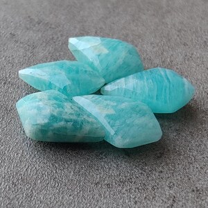 May include: Five smooth, light blue, faceted, gemstone beads. The beads are shaped like elongated diamonds.