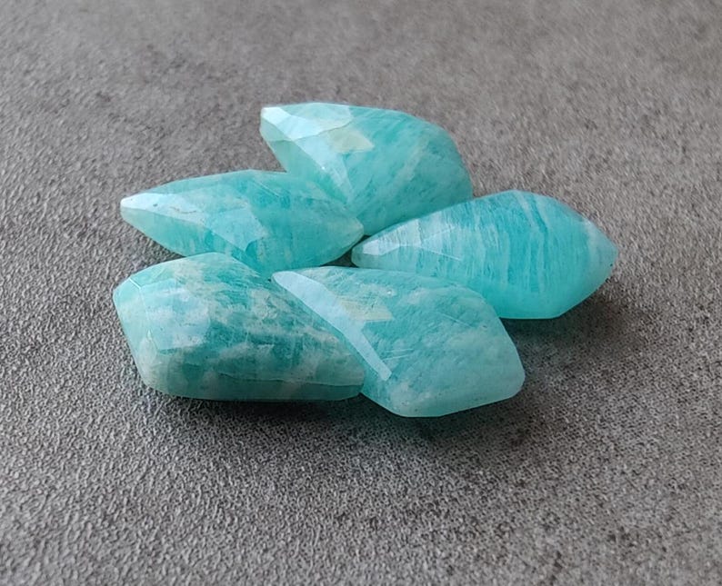 May include: Five smooth, light blue, faceted, gemstone beads. The beads are shaped like elongated diamonds.