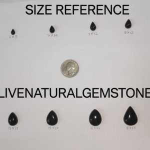 Op de afbeelding: Een verzameling zwarte, druppelvormige edelstenen in verschillende maten, gepresenteerd op een witte achtergrond. Een munt wordt gebruikt ter vergelijking. De tekst "SIZE REFERENCE" en "LIVENATURALGEMSTONE1" is zichtbaar.
