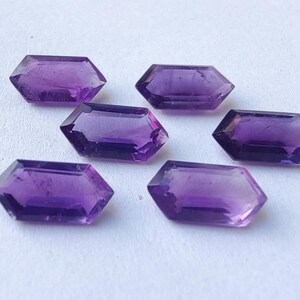 K&ouml;nnte beinhalten: Sechs facettierte, sechseckige Amethyst-Edelsteine. Die Edelsteine haben eine tiefviolette Farbe und sind auf einer wei&szlig;en Oberfl&auml;che angeordnet. Die Facetten fangen das Licht ein und erzeugen einen funkelnden Effekt. Geeignet f&uuml;r die Schmuckherstellung.