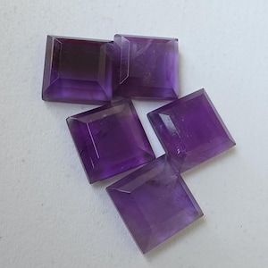 Peut inclure: Cinq pierres pr&eacute;cieuses d'am&eacute;thyste taill&eacute;es en carr&eacute;. Les pierres sont d'un violet profond avec un design &agrave; facettes. Les pierres sont dispos&eacute;es sur une surface blanche. Ces pierres sont adapt&eacute;es &agrave; la joaillerie.