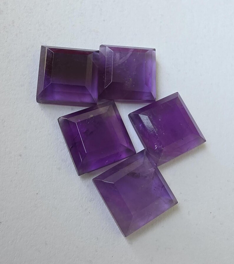 Peut inclure: Cinq pierres pr&eacute;cieuses d'am&eacute;thyste taill&eacute;es en carr&eacute;. Les pierres sont d'un violet profond avec un design &agrave; facettes. Les pierres sont dispos&eacute;es sur une surface blanche. Ces pierres sont adapt&eacute;es &agrave; la joaillerie.