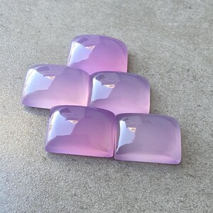 Pu&ograve; includere: Cinque pietre preziose lucide, color lavanda, con angoli arrotondati, sono disposte su una superficie grigia. Le gemme hanno una qualit&agrave; traslucida, riflettendo la luce e creando riflessi. Le pietre sono probabilmente per la creazione di gioielli o artigianato.