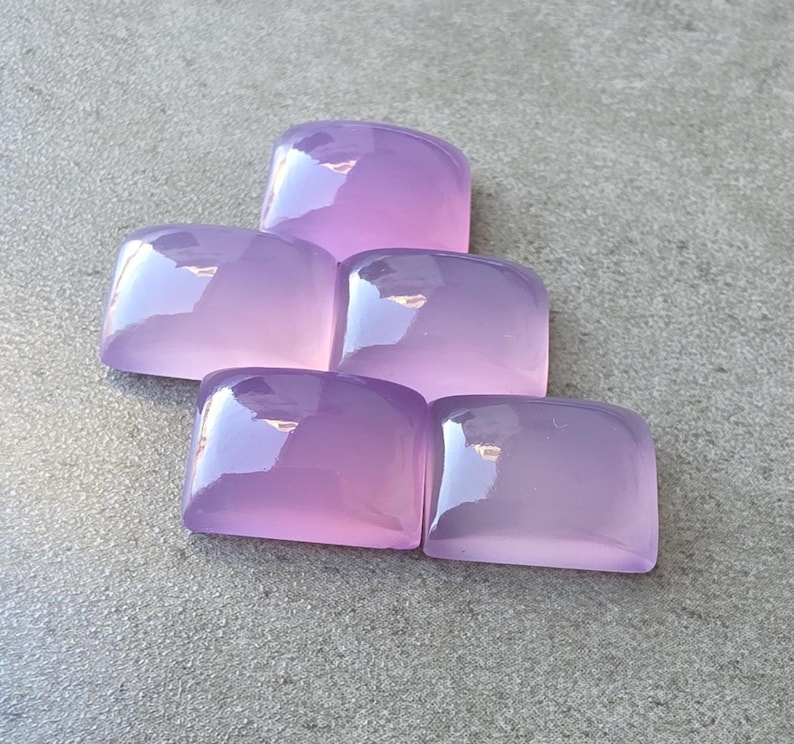 Pu&ograve; includere: Cinque pietre preziose lucide, color lavanda, con angoli arrotondati, sono disposte su una superficie grigia. Le gemme hanno una qualit&agrave; traslucida, riflettendo la luce e creando riflessi. Le pietre sono probabilmente per la creazione di gioielli o artigianato.