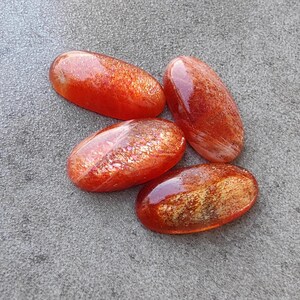 K&ouml;nnte beinhalten: Vier ovale Cabochons aus Sunstone in Orange- und Rott&ouml;nen mit schimmerndem, irisierendem Finish.