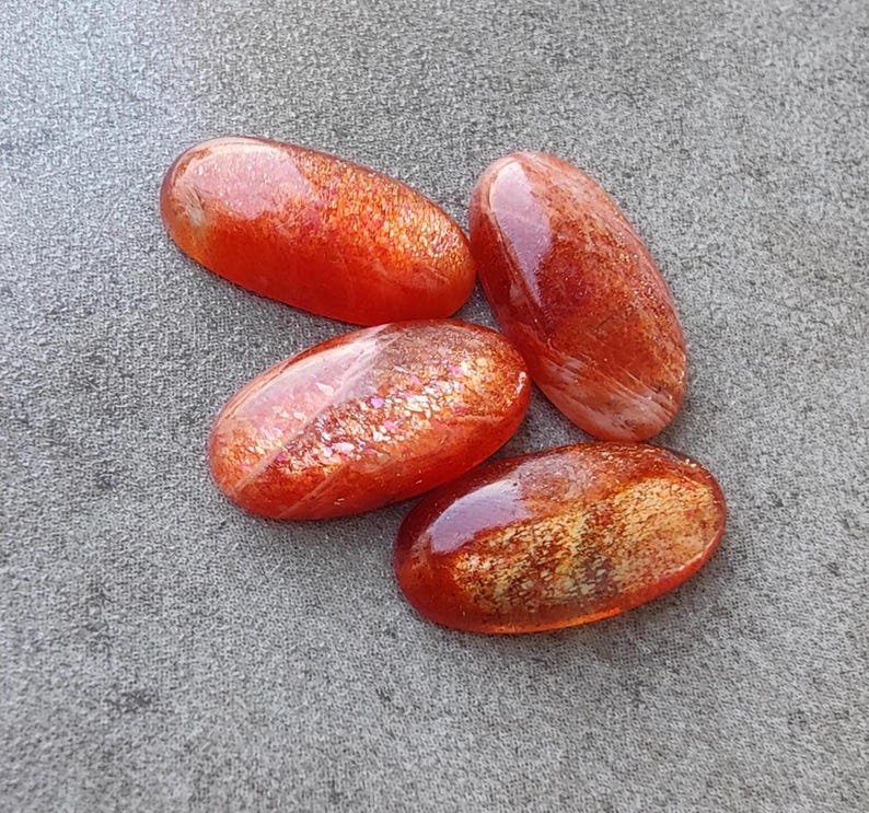 K&ouml;nnte beinhalten: Vier ovale Cabochons aus Sunstone in Orange- und Rott&ouml;nen mit schimmerndem, irisierendem Finish.