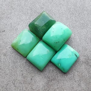 May include: Five green gemstone cabochons cut in a square shape. The gemstones are polished and have a smooth, shiny surface.