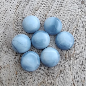 May include: Seven smooth, round, light blue opal cabochons. The opals have a white marbled pattern.