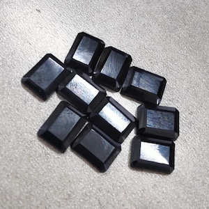 以下が含まれることがあります： 長方形の黒い宝石のコレクション。研磨された反射面があり、散らばったパターンで配置されています。暗い色と幾何学的な形状が特徴です。これらの宝石は、ジュエリー作りに使用される可能性があります。