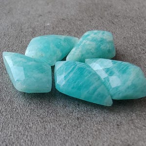 May include: Five smooth, faceted, light blue-green amazonite gemstones. The stones are irregularly shaped and have a translucent appearance.