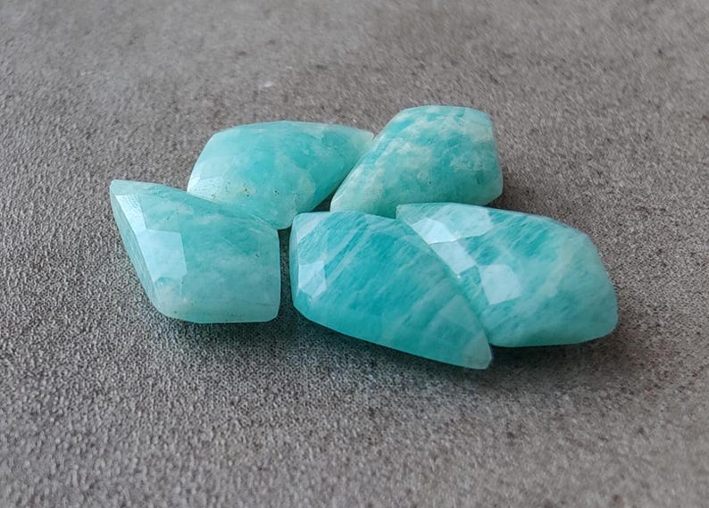 May include: Five smooth, faceted, light blue-green amazonite gemstones. The stones are irregularly shaped and have a translucent appearance.