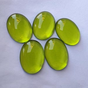 May include: Five oval-shaped, bright green glass cabochons. The cabochons are smooth and shiny.