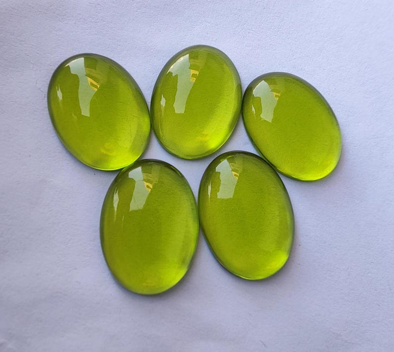 May include: Five oval-shaped, bright green glass cabochons. The cabochons are smooth and shiny.