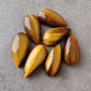 May include: Eight teardrop-shaped tiger's eye stones in shades of brown and gold. The stones are polished and have a glossy finish.