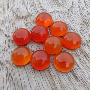 May include: Nine round, orange carnelian gemstones on a light wood surface.